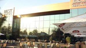 Ένας εξωτερικός χώρος με τραπέζια και καρέκλες, μια πινακίδα που αναγράφει «Καλύτερο Ξενοδοχείο» και, στο βάθος, ένα εστιατόριο με το όνομα «Ajuste Aloha».