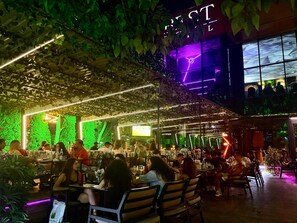 An indoor dining area with tables and chairs, surrounded by greenery and illuminated by neon lights. - Best Hotel (Ploiesti)