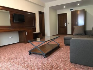 A living room with a sofa, a glass-top coffee table with wheels, a TV mounted on a wooden wall, and a wardrobe. - Best Hotel (Ploiesti)