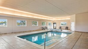 Una piscina interior con ventanales amplios, suelo de baldosas y algunas sillas cerca de la piscina.