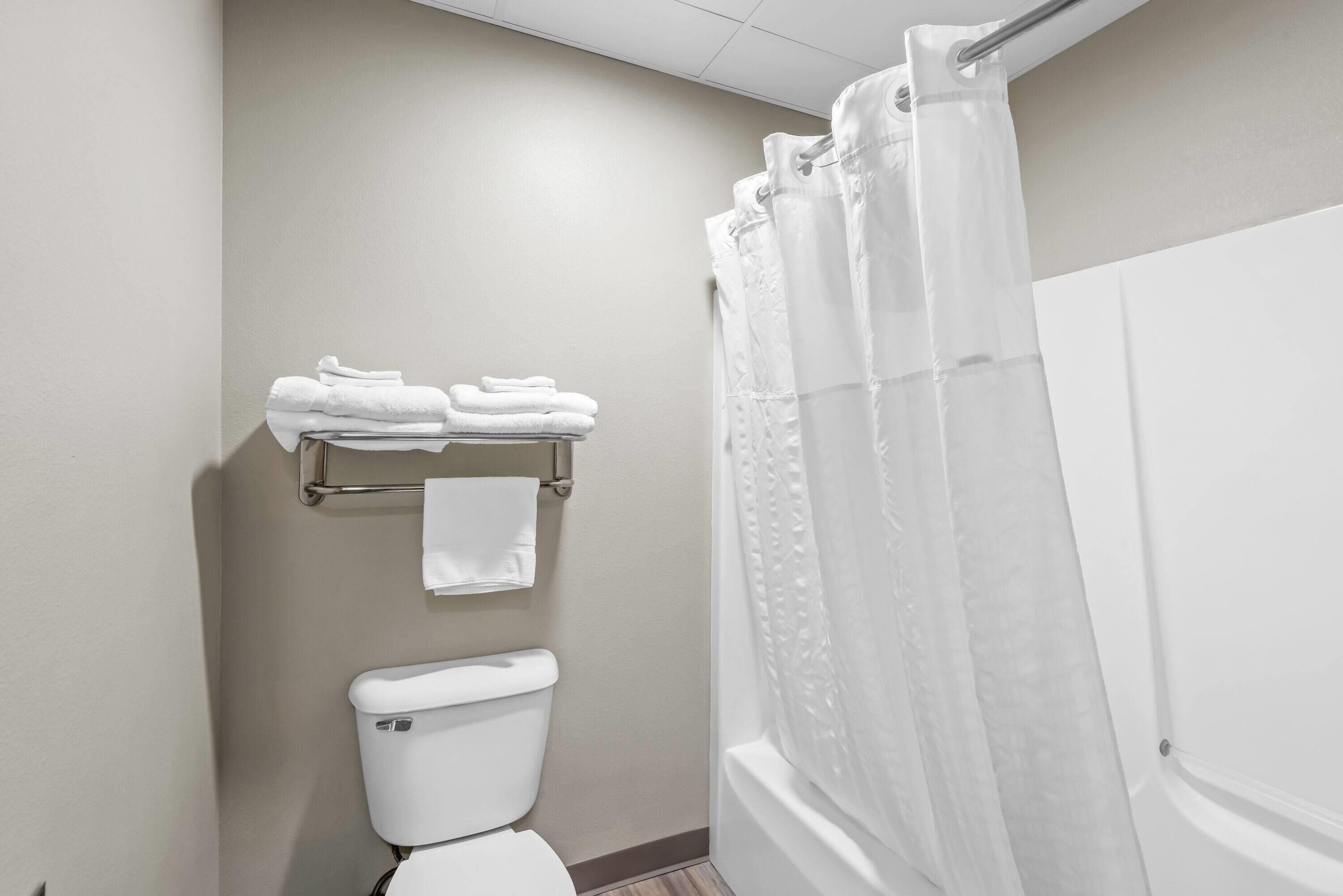 A bathroom with a toilet, a towel rack with folded towels, and a shower curtain.