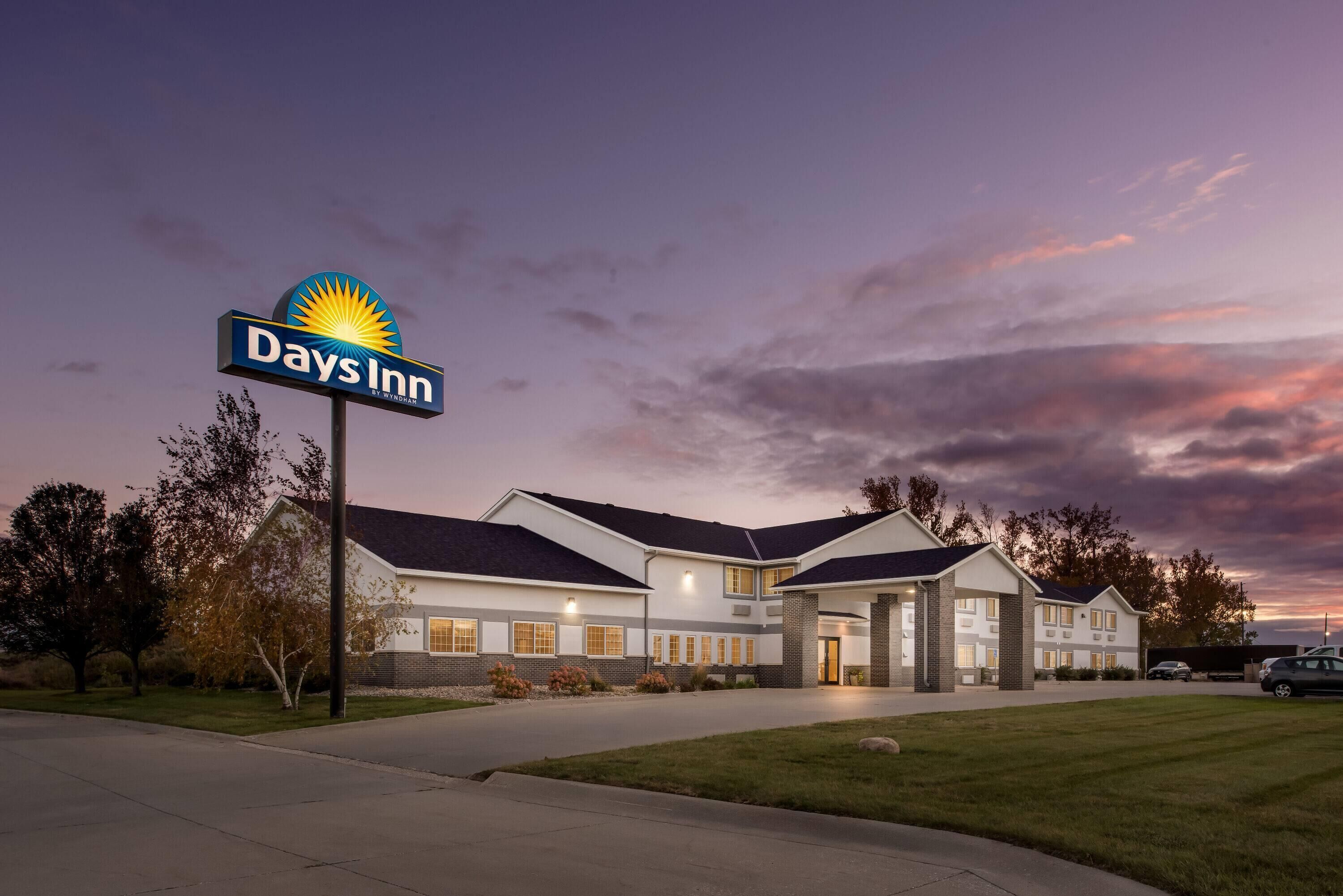 Un hotel Days Inn con un diseño moderno, que presenta un gran letrero con el logotipo de Days Inn, un césped bien cuidado y un área de estacionamiento.