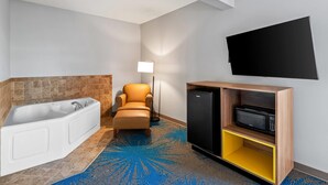 Un baño con bañera, una silla, una lámpara de pie, un microondas y un televisor montado en la pared.