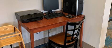 Habitación de hotel con un escritorio de madera, una computadora, una silla, un taburete pequeño de madera y piso alfombrado.