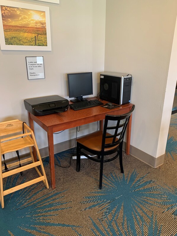 Habitación de hotel con un escritorio de madera, una computadora, una silla, un taburete pequeño de madera y piso alfombrado.