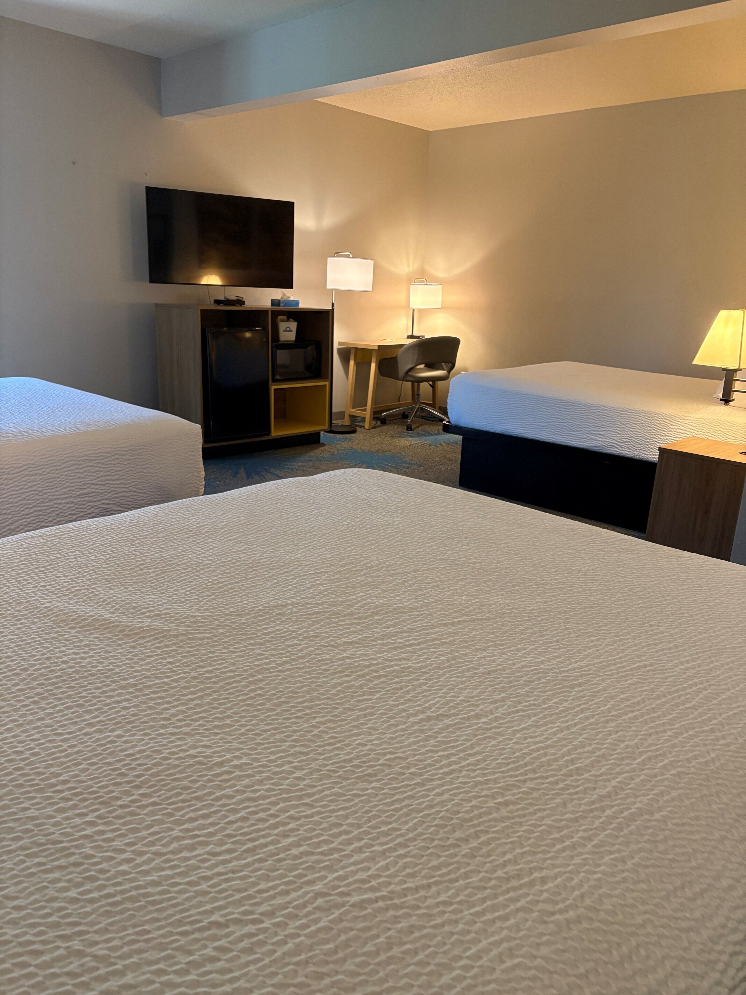 A hotel room with two beds, a desk, a chair, a television, and two lamps.