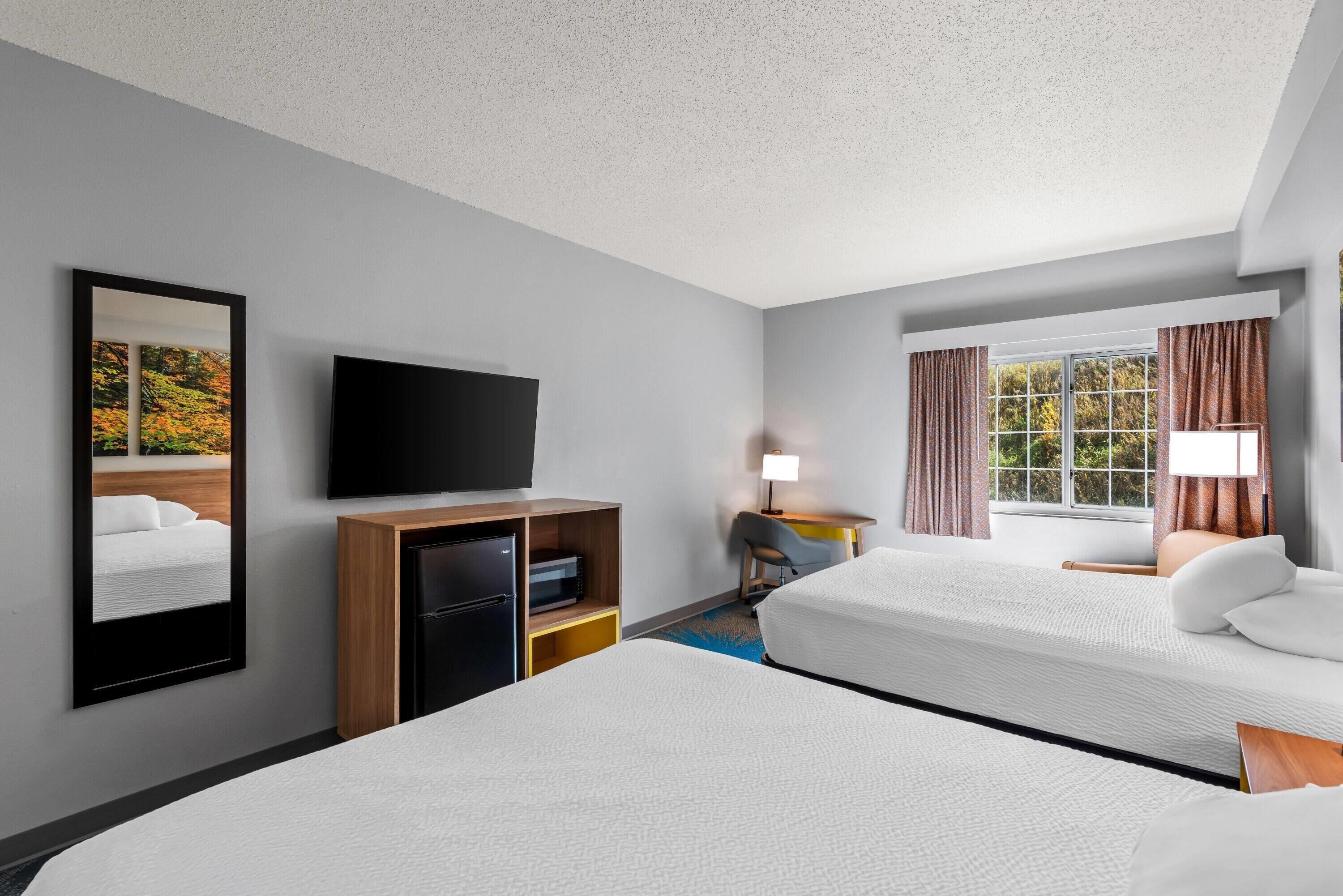 Habitación de hotel con dos camas, un televisor de pantalla plana, un escritorio con lámpara y una ventana con cortinas.