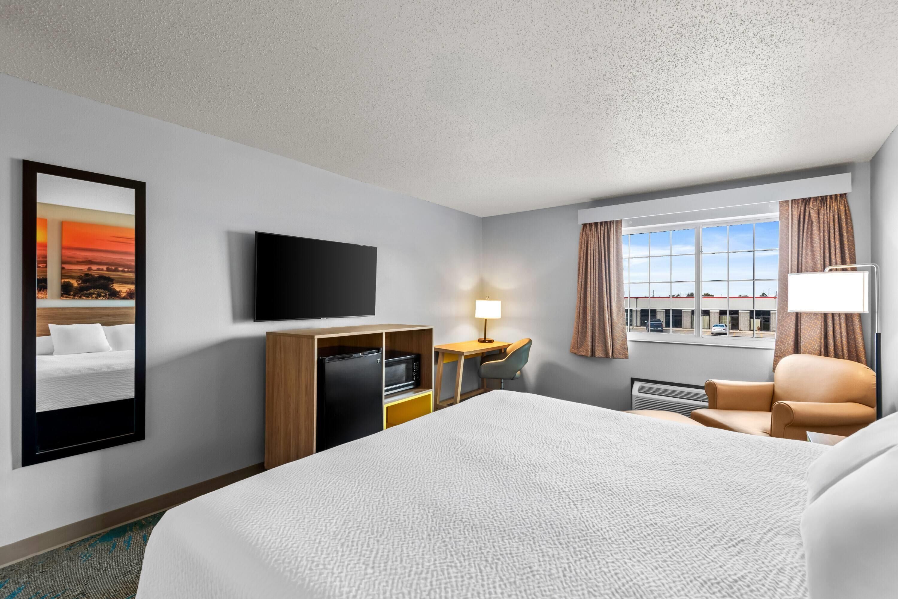 A hotel room with a bed, a desk with a chair, a television, and a window with curtains.