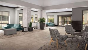 Un vestíbulo amplio con un sofá color turquesa, sillones estampados y una planta grande en maceta.