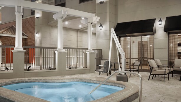 Una piscina interior con borde de azulejos, una escalera y una zona de estar con sillas y una mesa.