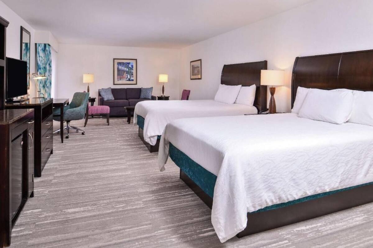 A hotel room with two beds, a desk, a chair, and a television.