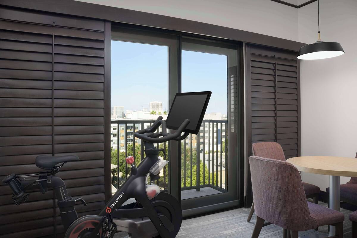 A modern room with a large sliding glass door leading to a balcony, a stationary exercise bike, a round table, and a single chair.