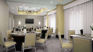 A conference room with a large round table, multiple chairs, a flat-screen TV, and a ceiling light fixture.