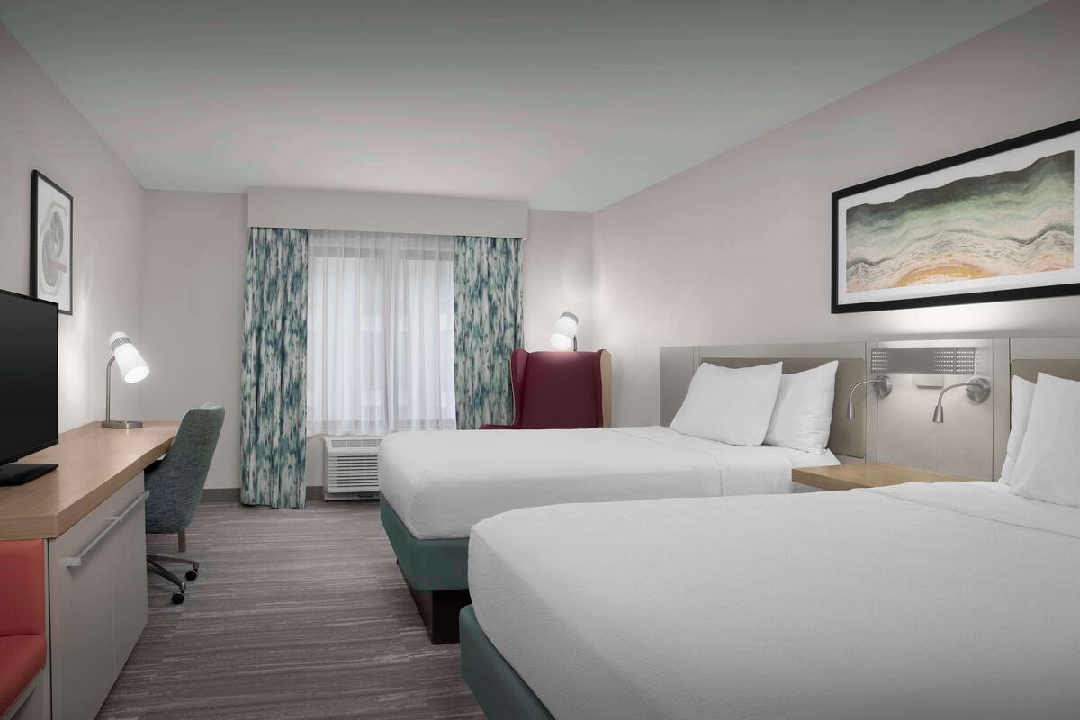 A hotel room with two beds, a desk, a chair, a television, and a painting on the wall.