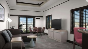 Una sala de estar moderna con un sofá, una mesa de comedor y sillas. Hay un televisor sobre un mueble bajo y se observa un ventilador de techo.