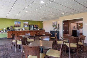 A hotel dining area with multiple tables and chairs, a kitchen in the background, and a view of the outside. - Sleep Inn & Suites Oakley I-70 (Oakley)