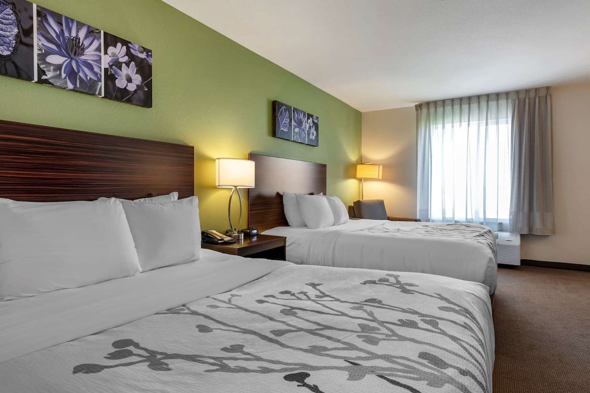A hotel room with two beds, a wooden headboard, bedside lamps, and artwork on the walls.