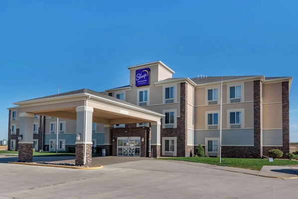 A Sleep Inn & Suites building with a covered entrance, multiple windows, and a clear blue sky. - Sleep Inn & Suites Oakley I-70 (Oakley)