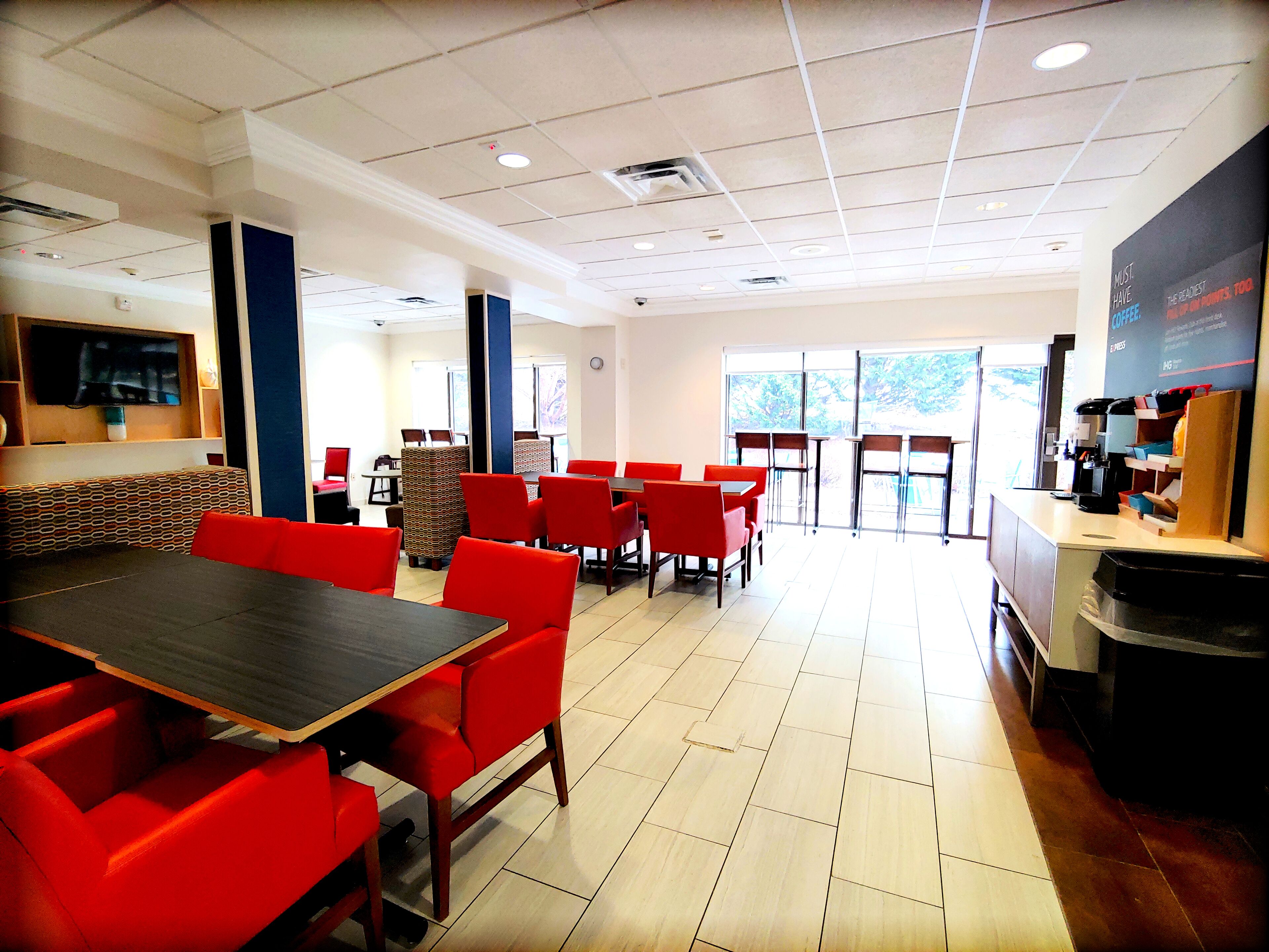 A spacious dining area with red chairs and tables, a flat-screen TV mounted on the wall, and a coffee machine on the counter.