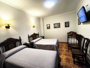 Une chambre d’hôtel avec deux lits simples, une chaise en bois, un téléviseur fixé au mur et deux lampes murales.