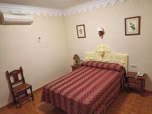 A bedroom with a bed, a chair, a nightstand, a lamp, and a wall-mounted air conditioner. - Bellido (Montilla)
