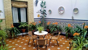 A courtyard with a tiled floor, potted plants, a table with chairs, and decorative plates on the wall. - Bellido (Montilla)