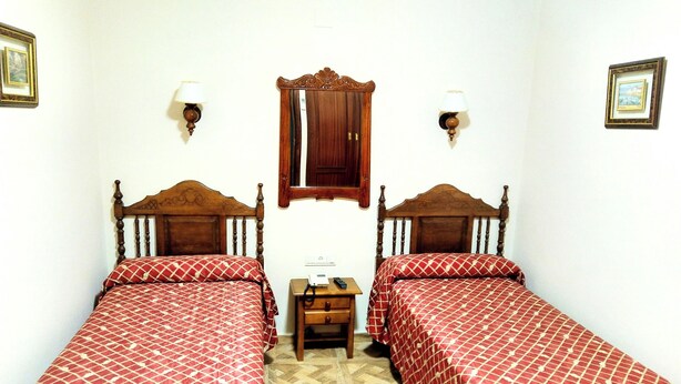 A room with two wooden beds, a small wooden nightstand, a mirror, and two wall-mounted lamps. - Bellido (Montilla)