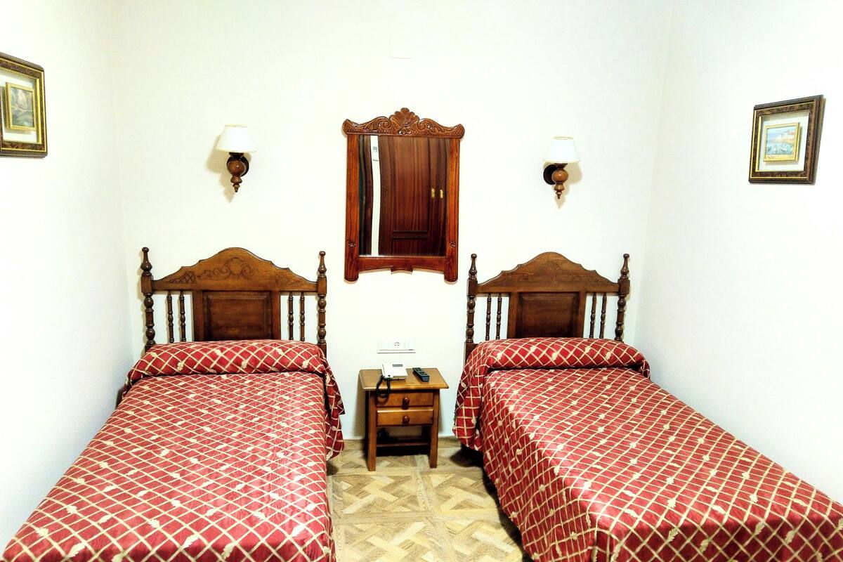 A room with two wooden beds, a small wooden nightstand, a mirror, and two wall-mounted lamps.