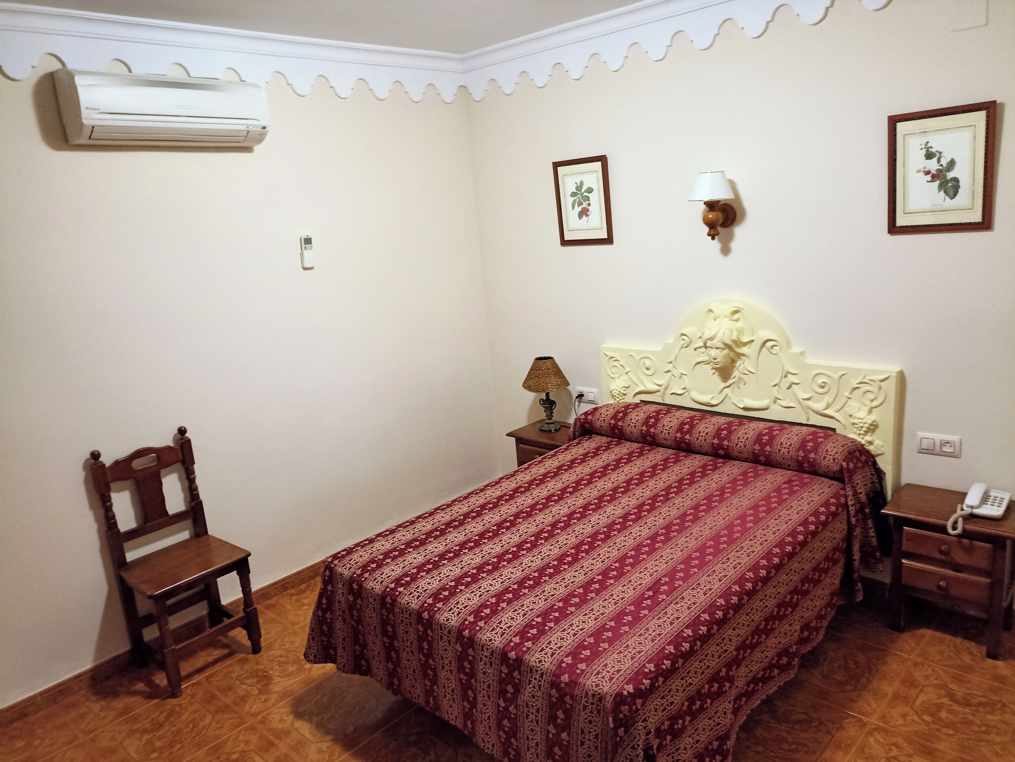 Un dormitorio con cama, una silla, una mesita de noche, una lámpara y un equipo de aire acondicionado.