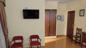 A room with two wooden chairs, a television mounted on the wall, and a wooden door. - Bellido (Montilla)