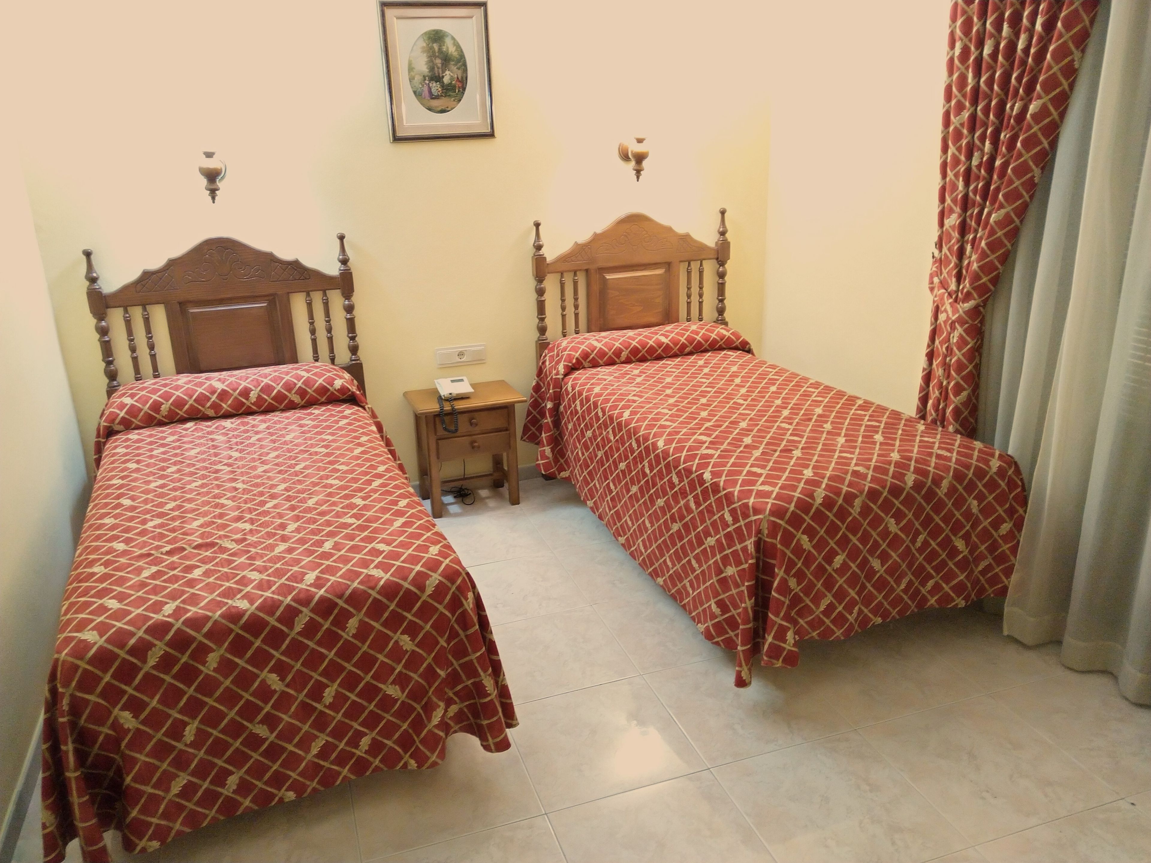Une chambre d’hôtel avec deux lits simples, une table de chevet, une lampe fixée au mur et un tableau encadré.