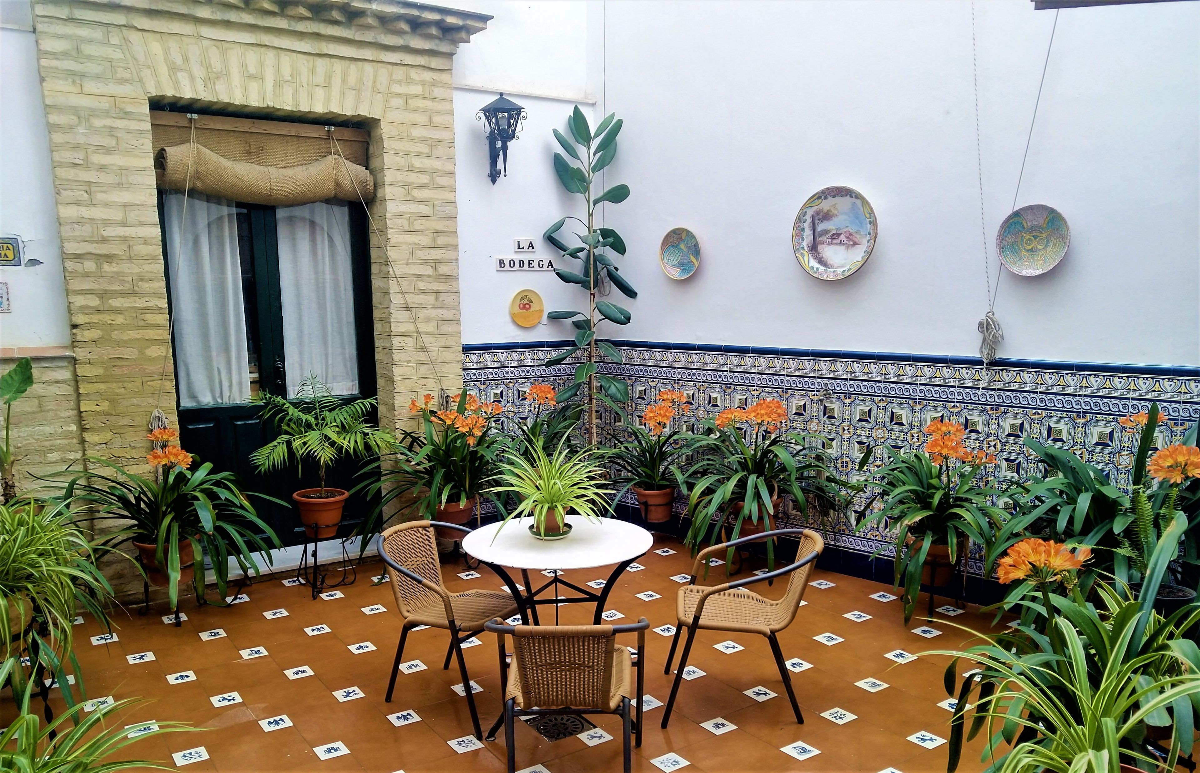 Een terras met een tafel en stoelen, omringd door plantenpotten en een betegelde muur met decoratieve borden.