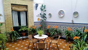 Een terras met een tafel en stoelen, omringd door plantenpotten en een betegelde muur met decoratieve borden.