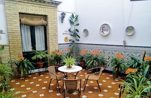 A patio with a table and chairs, surrounded by potted plants and a tiled wall with decorative plates. - Bellido (Montilla)