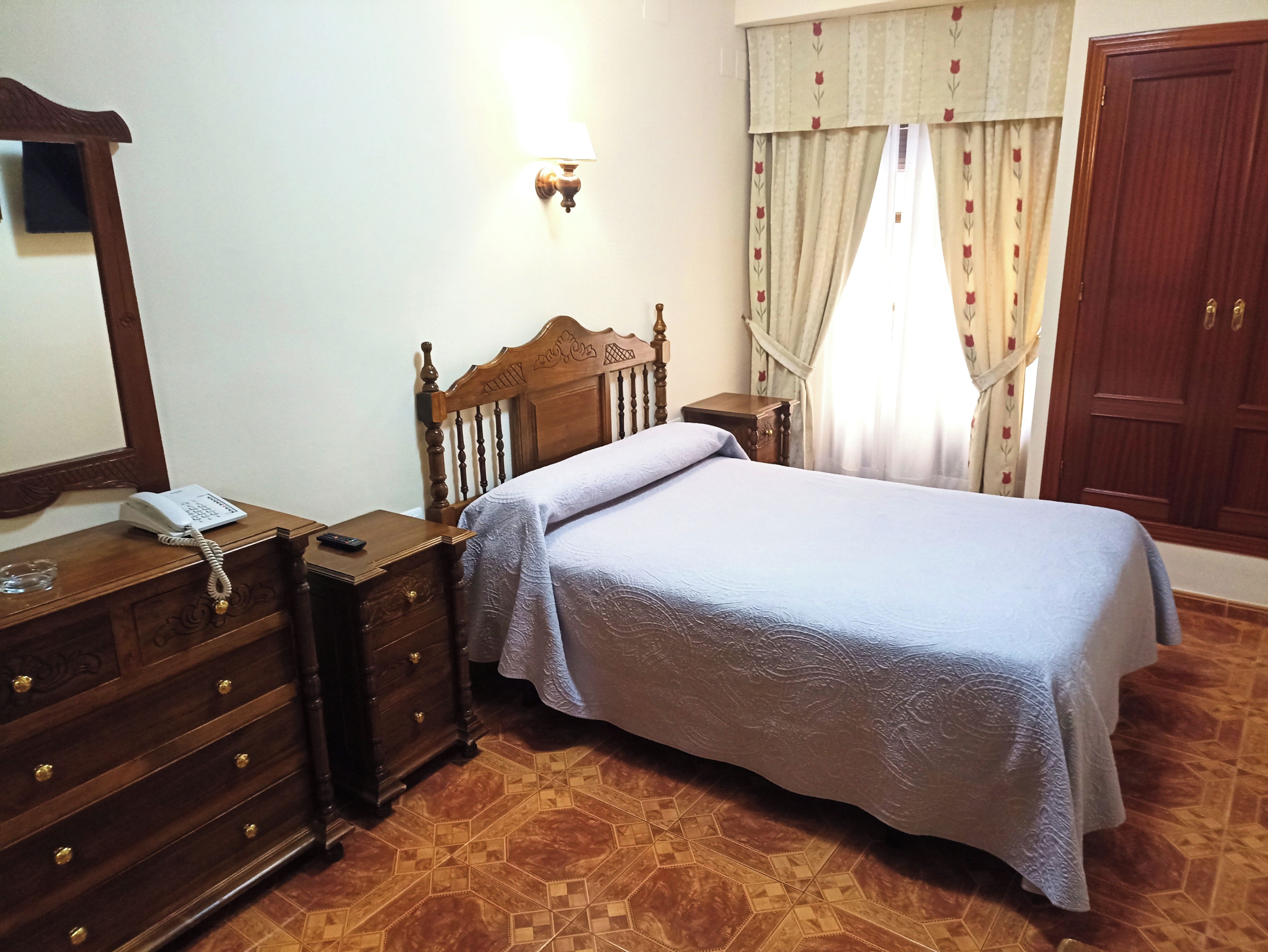 Een slaapkamer met een houten bed, een nachtkastje met een lamp, een dressoir en een spiegel.