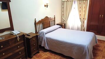 Een slaapkamer met een houten bed, een nachtkastje met een lamp, een dressoir en een spiegel.