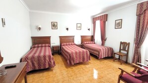 A hotel room with three single beds, a wooden desk, a chair, and a small table. - Bellido (Montilla)