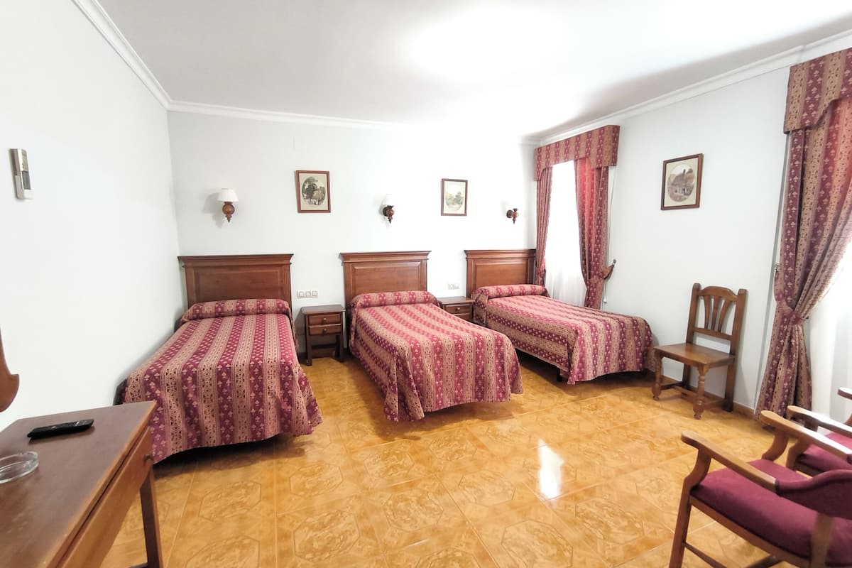 Une chambre d’hôtel avec trois lits simples, un bureau en bois, une chaise et une petite table.