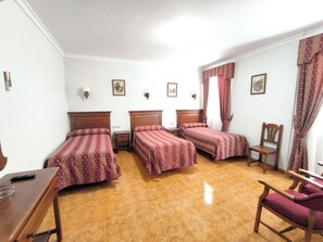 A hotel room with three single beds, a wooden desk, a chair, and a small table. - Bellido (Montilla)
