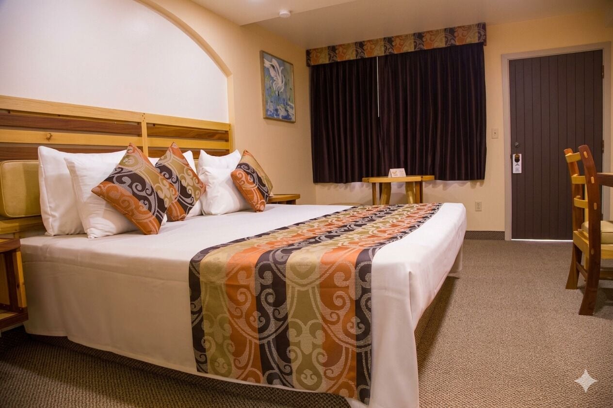 Ein Hotelzimmer mit Bett, kleinem Tisch, Stuhl, einem Bild an der Wand und einer Tür.