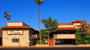 Un hôtel appelé «Hotel La Villa », avec une enseigne indiquant «Hôtel » au-dessus de l’entrée, un palmier devant et un toit recouvert de tuiles rouges.
