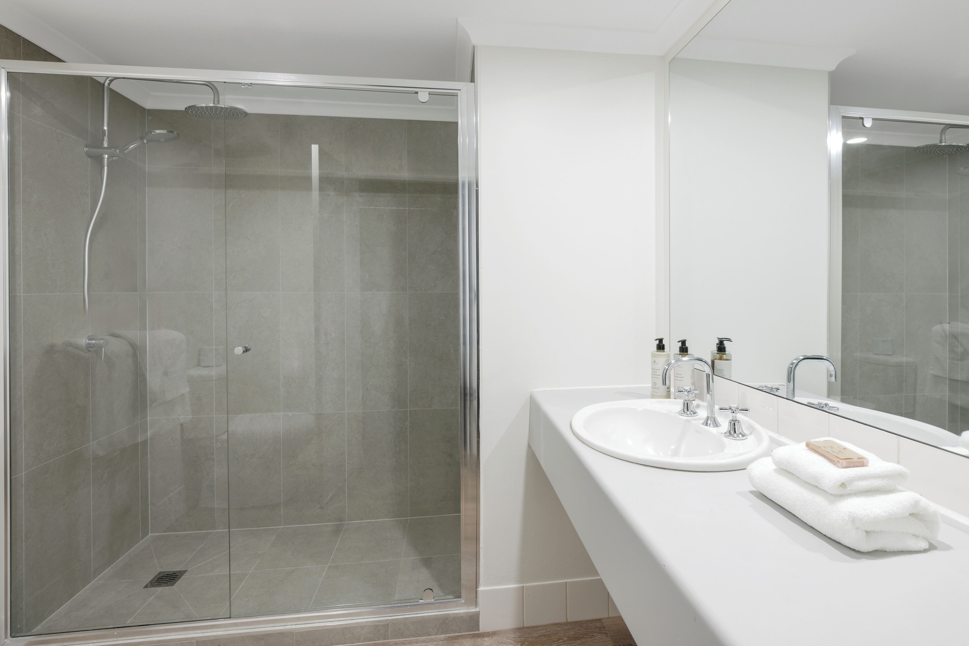 A modern bathroom with a glass-enclosed shower, a white sink with a mirror, and neatly folded towels.