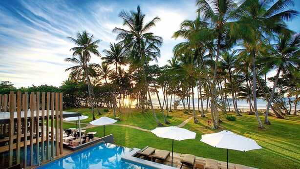 A poolside area with lounge chairs and umbrellas, surrounded by palm trees and a view of the ocean. - Club Wyndham Mission Beach (Mission Beach)