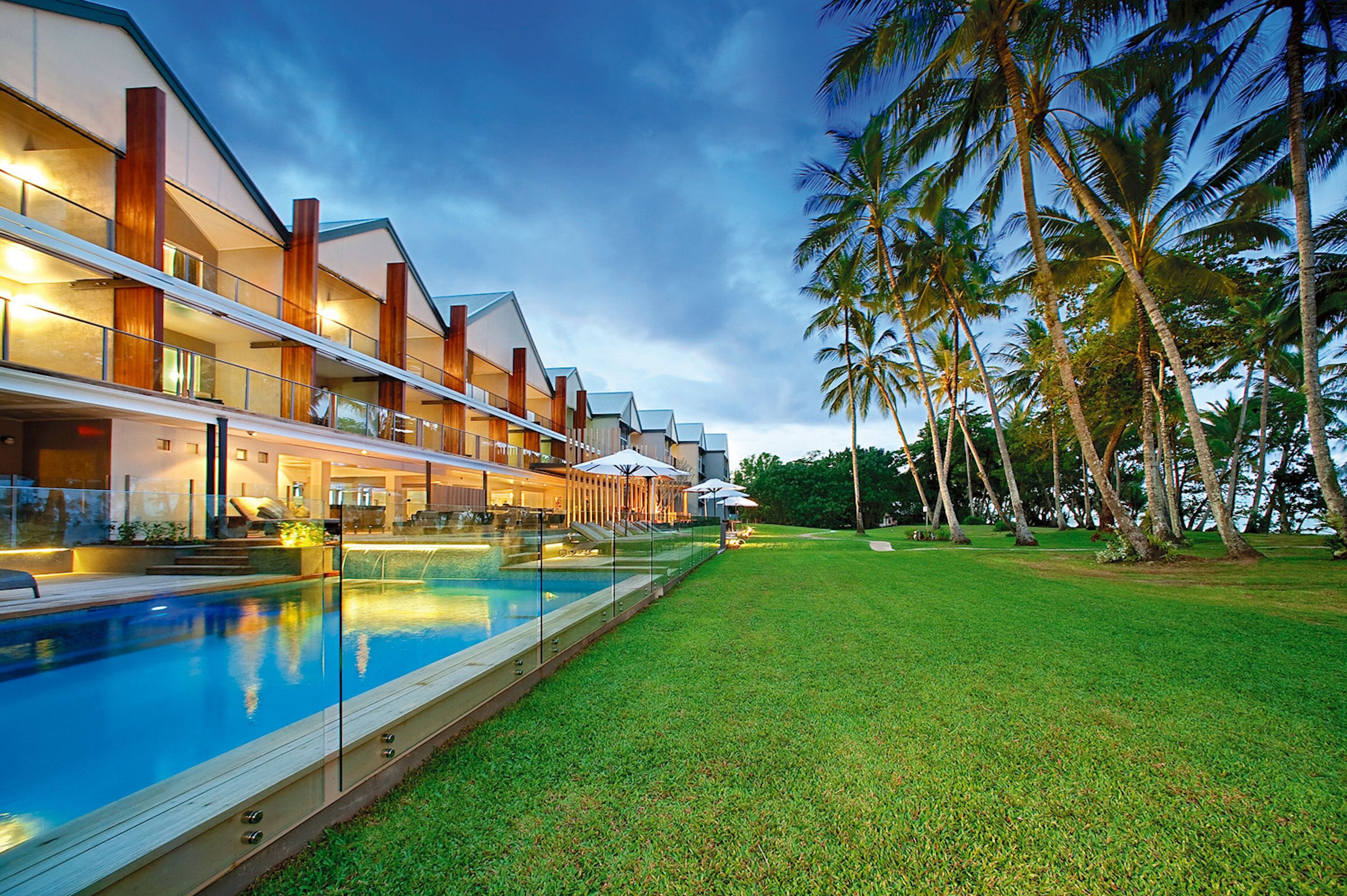 A modern hotel with a swimming pool, outdoor seating, and palm trees.