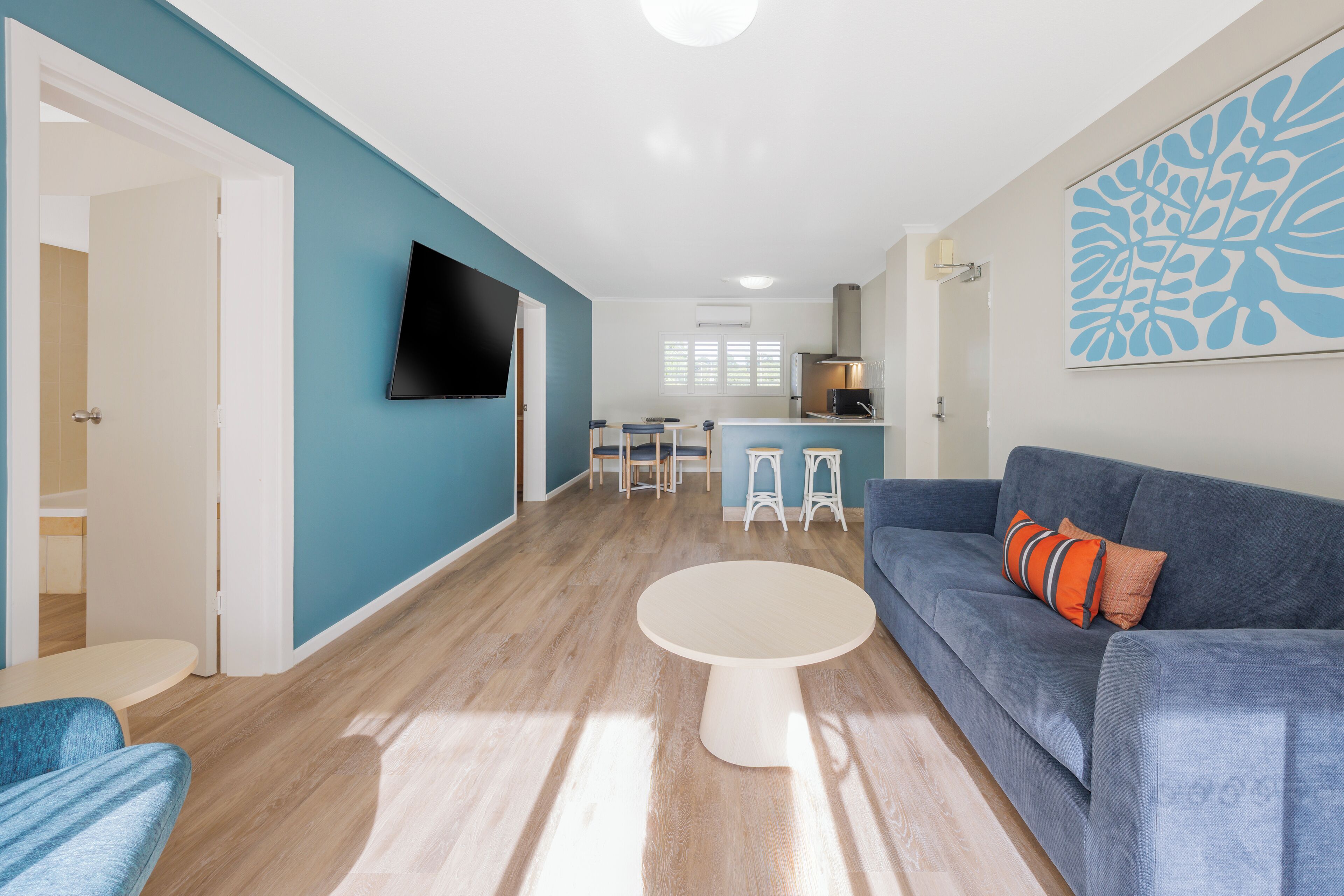 Uma sala de estar moderna com um sofá azul, uma mesa de centro redonda e uma TV fixada na parede.