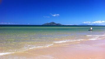 A beach with clear turquoise water, a sandy shore, and a distant mountain.