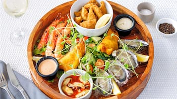 A wooden serving tray with various seafood dishes, including shrimp, oysters, and fried items, accompanied by small bowls of sauces and lemon wedges.