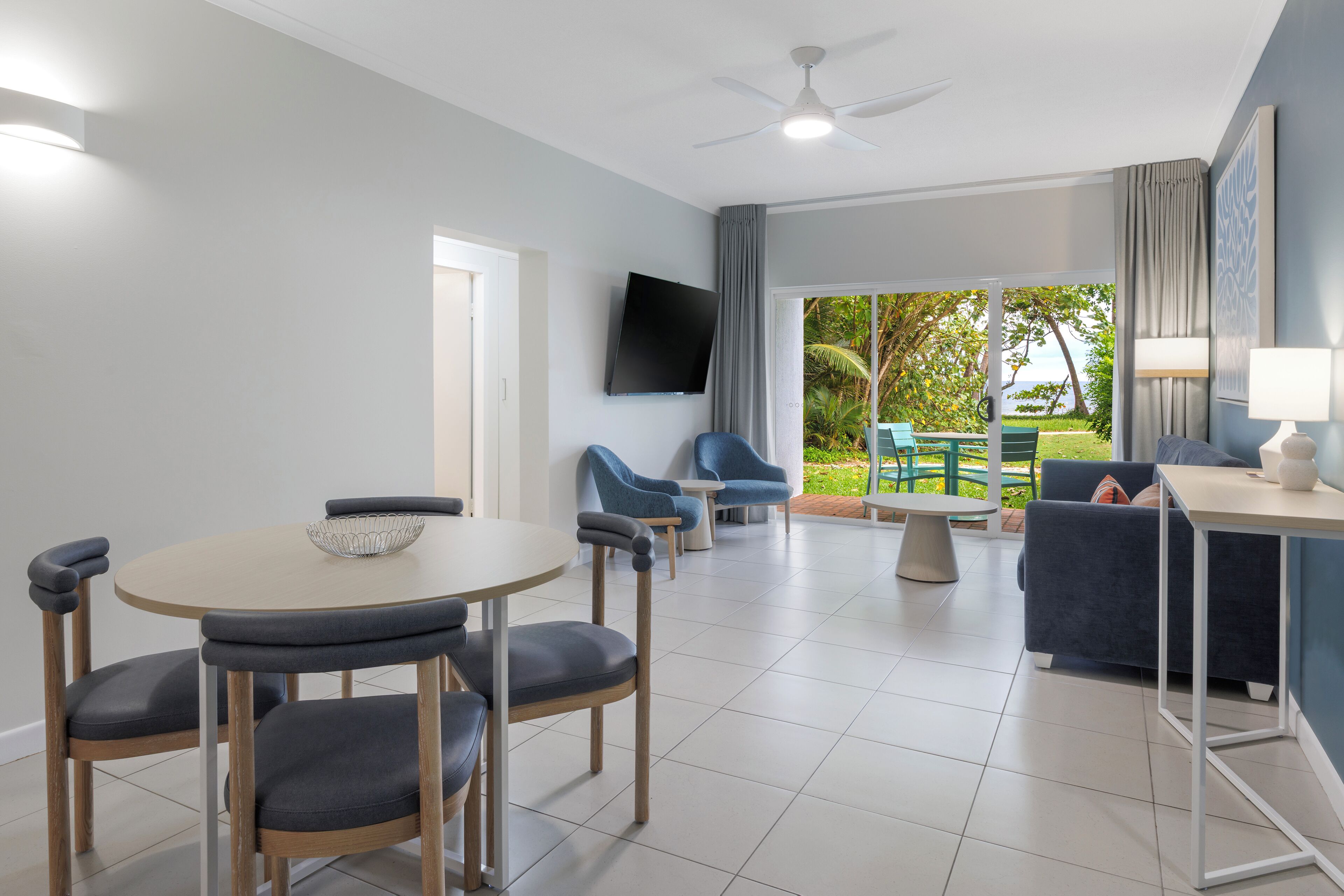 A modern living room with a dining area, a flat-screen TV, and a view of the outdoors.