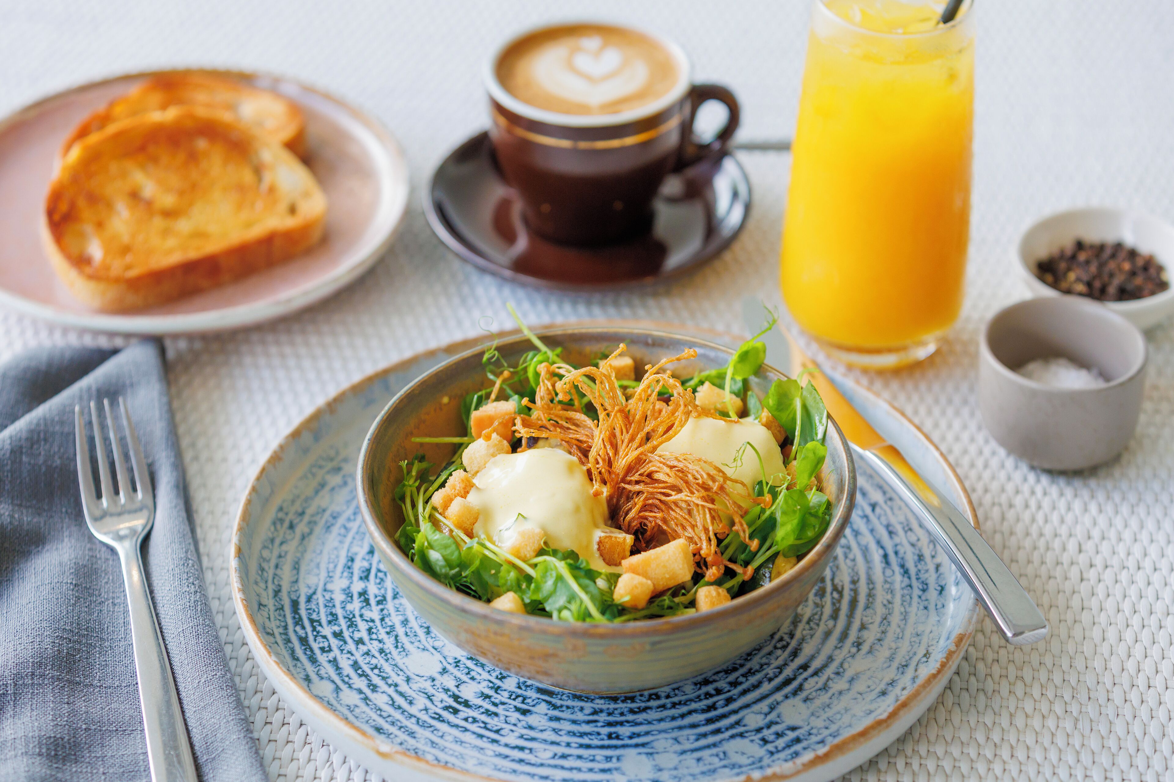 A breakfast setting with a bowl of salad, toast, a cup of coffee, and a glass of orange juice.