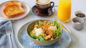 A breakfast setting with a bowl of salad, toast, a cup of coffee, and a glass of orange juice.